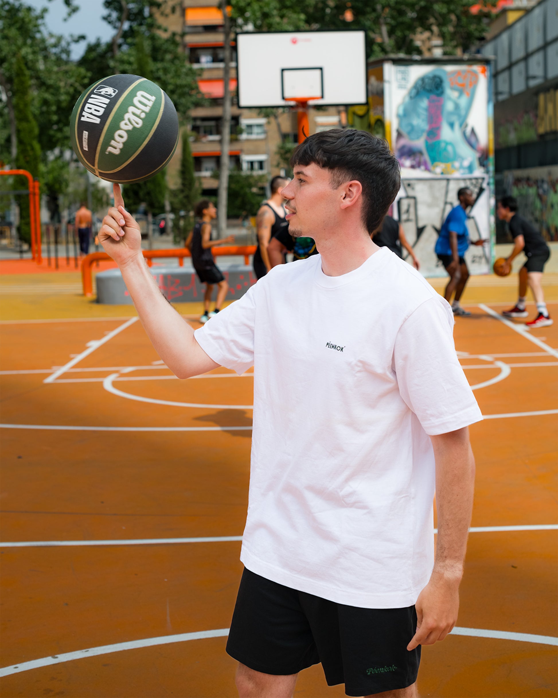 PÉENKOK' | ORGANIC COTTON SUSTAINABLE FASHION WHITE EMBROIDERED T-SHIRT WORN BY A MAN WITH A BASKETBALL ON HIS FINGER