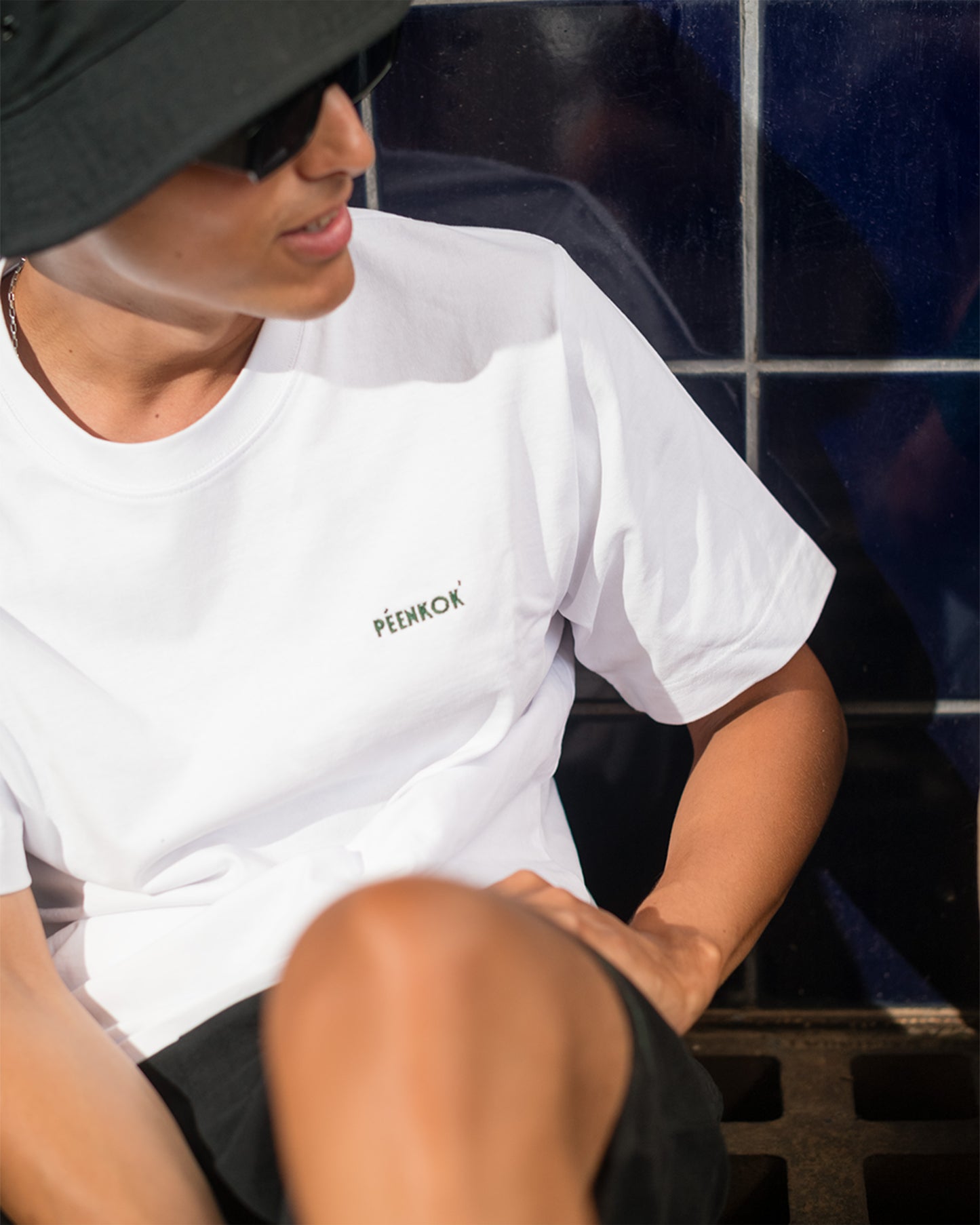 PÉENKOK' | ORGANIC COTTON SUSTAINABLE FASHION WHITE EMBROIDERED T-SHIRT WORN BY A MAN WITH A BLACK BUCKET HAT