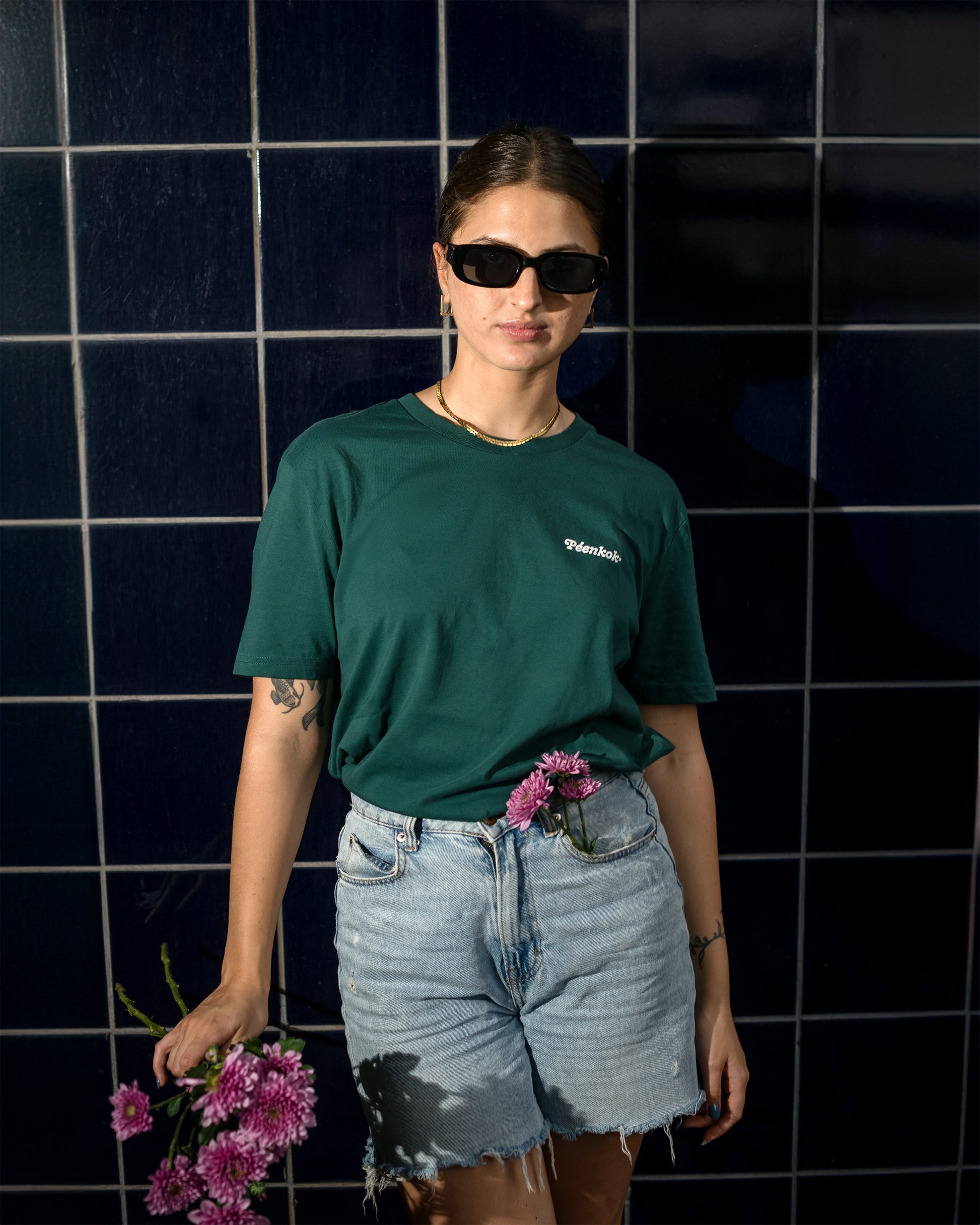 PÉENKOK' | GREEN ORGANIC COTTON SUSTAINABLE FASHION TEE WORN BY A WOMAN WITH A BOUQUET OF FLOWERS