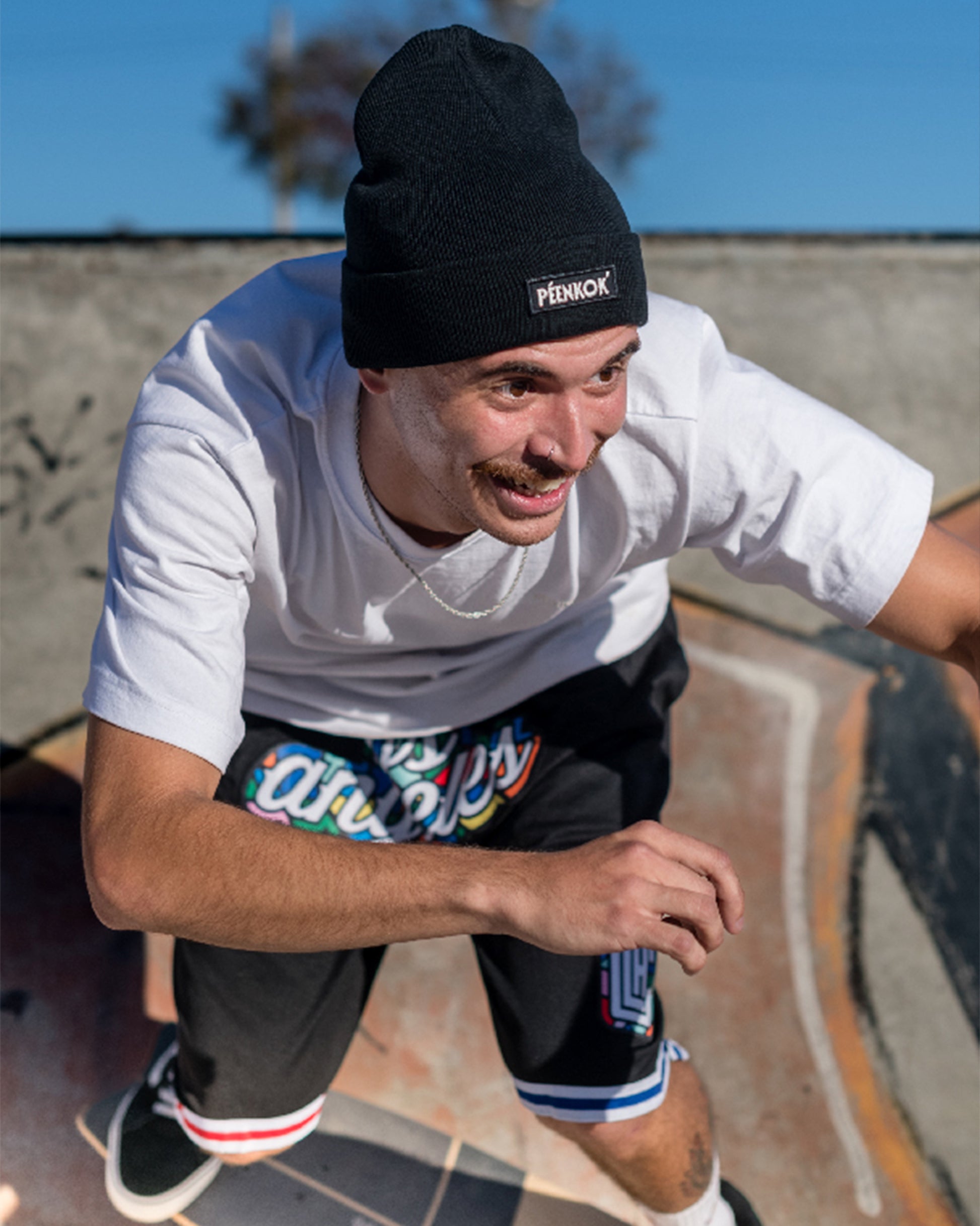 PÉENKOK’ | ORGANIC COTTON BEANIE BLACK WITH A WOVEN PATCH IN RECYCLED POLYESTER EMBROIDERY ON THE FRONT WORN BY A MAN SKATING