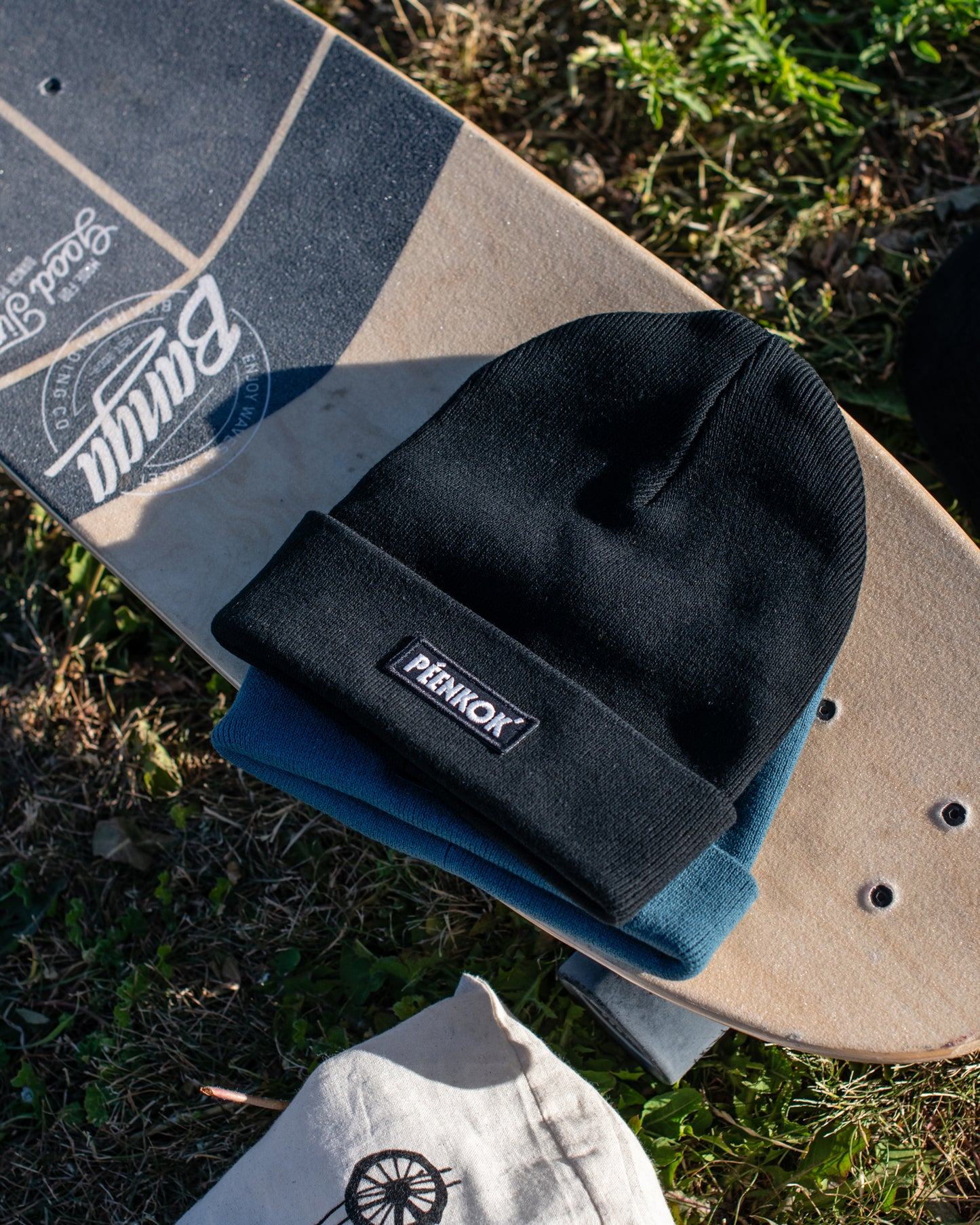 PÉENKOK’ | ORGANIC COTTON BEANIE BLACK WITH A WOVEN PATCH IN RECYCLED POLYESTER EMBROIDERY ON THE FRONT ON A SKATEBOARD.